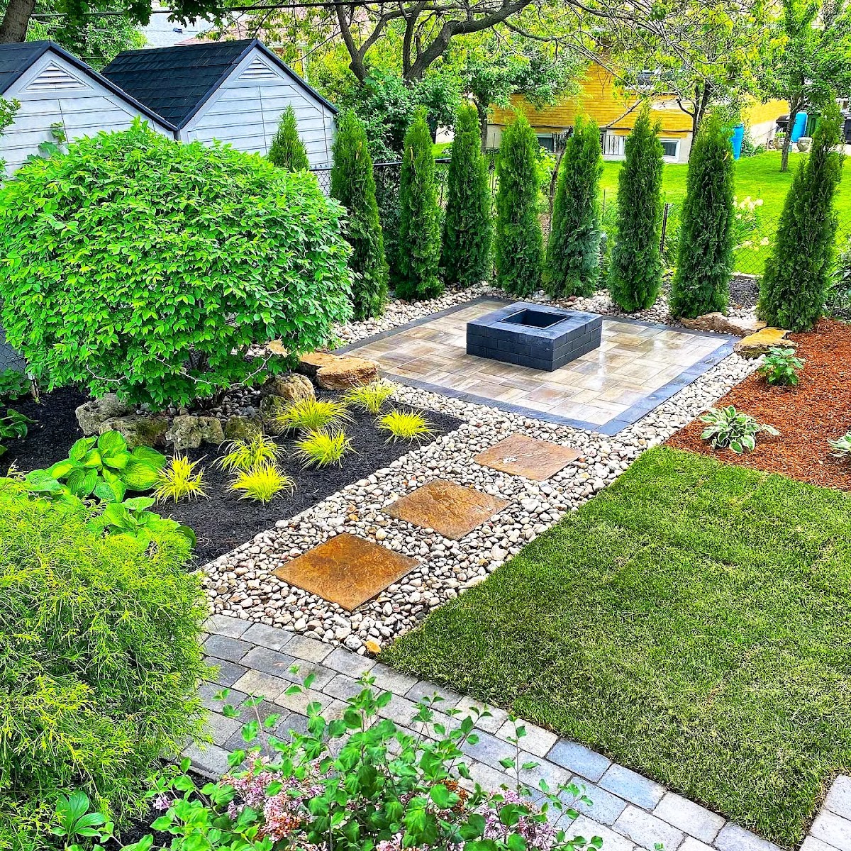 Backyard landscape with square fire pit patio, cedar privacy row, and river rock walkway